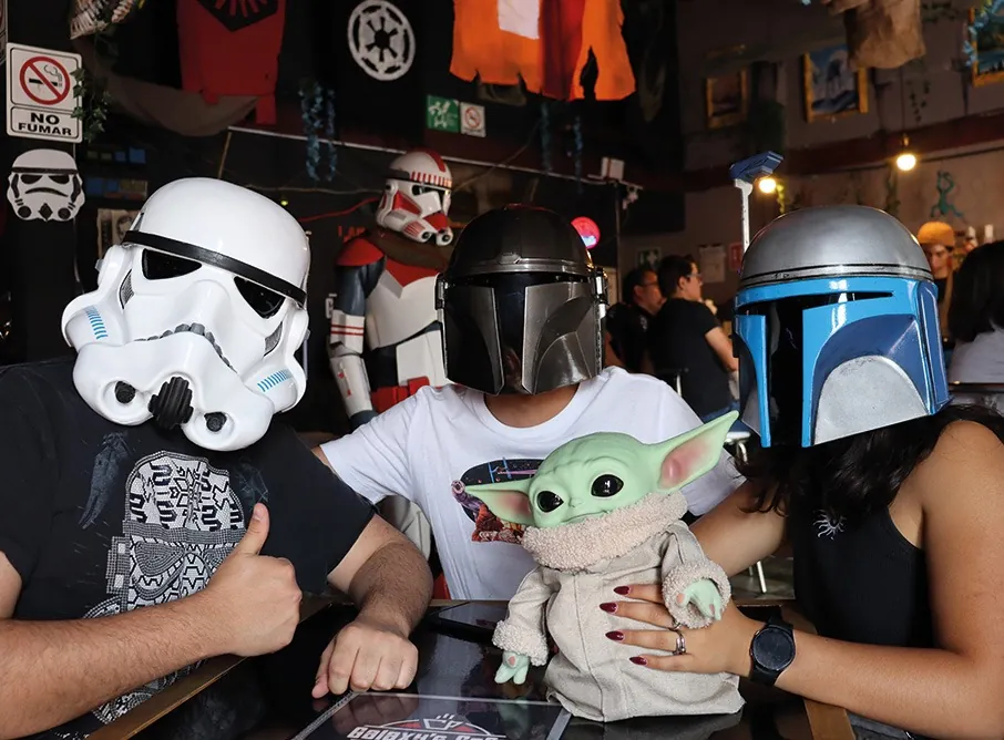 Amigos con cascos de soldado imperial y mandalorianos sostienen un muñeco de Grogu